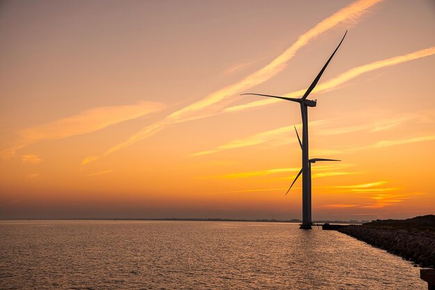 Wind turbines at sunset. Green ecological power energy generation. Wind farm eco field. Offshore and onshore windmill farm green energy at sea.