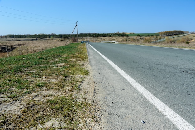 A winding highway stretching into the distance against the backdrop of a beautiful spring landscape, fields, meadows, forests and hills. Road stripes on asphalt. The prospect of going on a road trip.