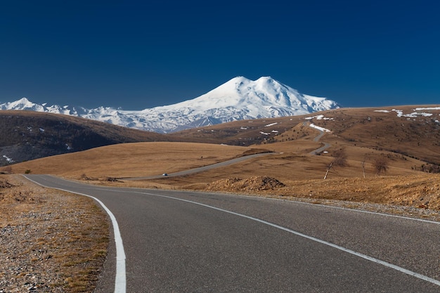 Winding road leads through hills to snowy mountains against clear blue sky Caucasus Russia