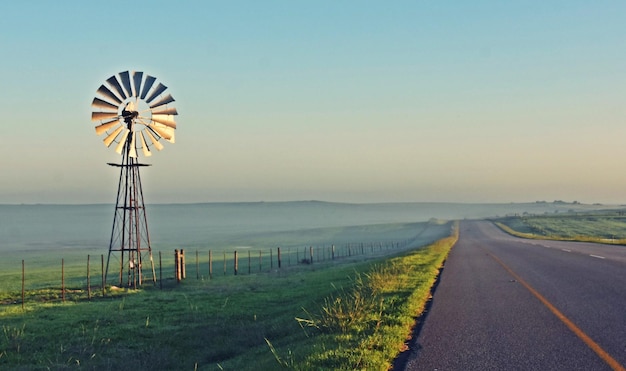 A Windmill water pump and a county road with morning fog