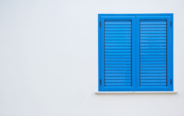 Window with blue shutters on a white wall. Window with closed shutters. Blue window in the wall of the house.