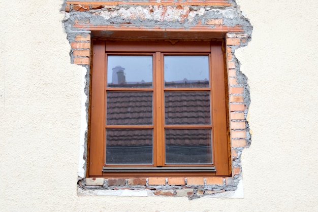 Window with brown frame on the background of the old white destroyed wall