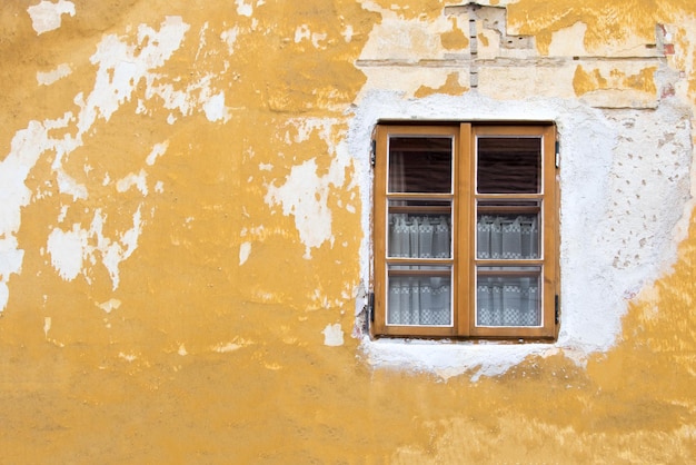 Window with brown frame on the background of the old yellow destroyed wall