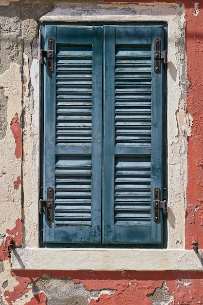 Window with closed old green green shutter on red wall. Italy, Venice, Burano island.