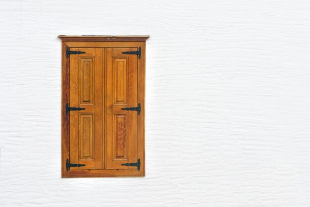 Window with wooden closed shutters against a white wall