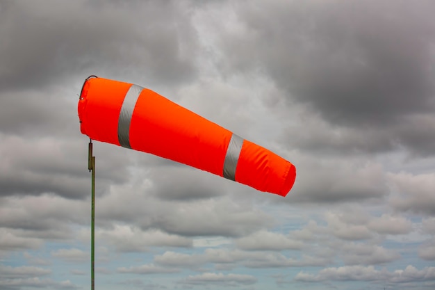 Windsock indicator of wind on tank chemical cone indicating wind direction and force. Horizontally flying windsock (wind vane) with cloud sky in the background.