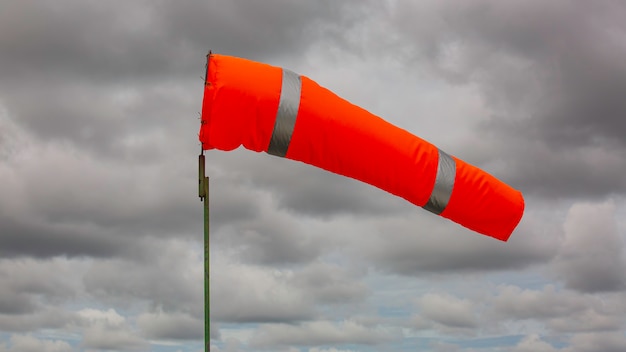 Windsock indicator of wind on tank chemical cone indicating wind direction and force. Horizontally flying windsock (wind vane) with cloud sky in the background.