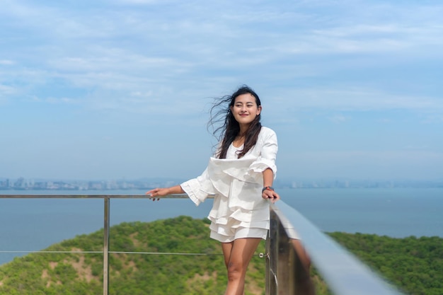 Windy hair Asian woman standing and looking forward with happiness at terrace view point