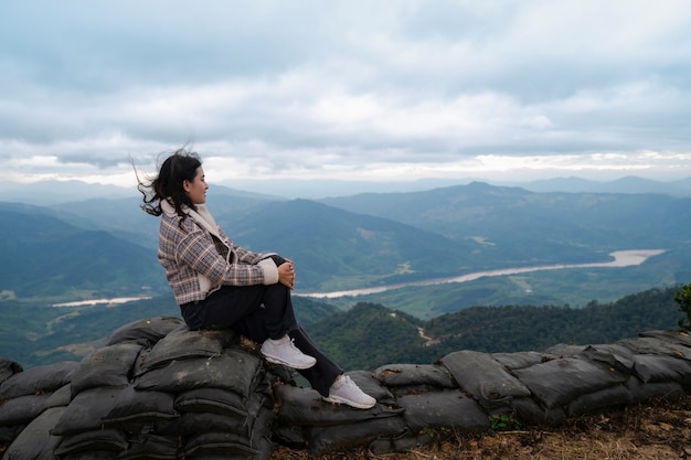 Windy hair woman sit and watching at view of Khong river and mountain in fog at Pha Tang viewpoint