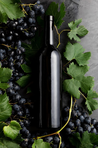 Wine bottle grapes, grape bunches with leaves and vines corkscrew on dark rustic concrete background. Flat lay wine composition on black stone table.