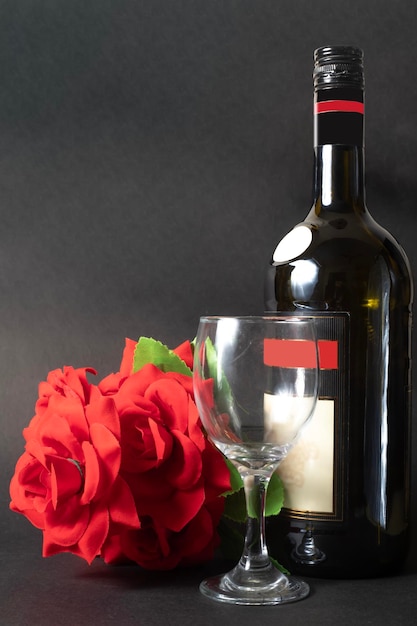 Photo wine bottle with a glass and a red rose on a black background