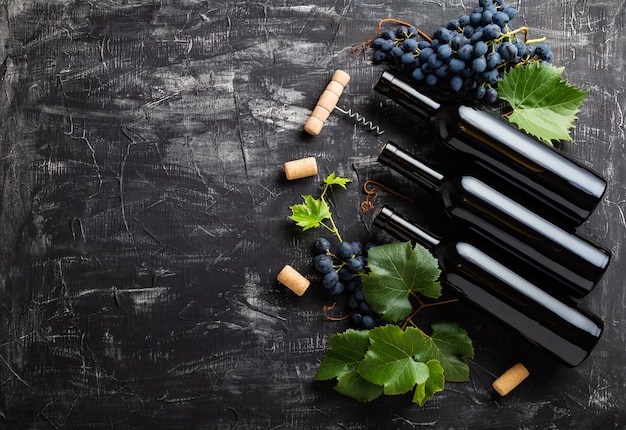 Wine bottles, grapes, grape bunches with leaves and vines corkscrew wine corks on dark rustic concrete background. Flat lay wine composition with copy space on black stone table.