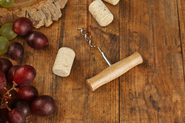 Wine corks and tailspin with grapes on wooden background