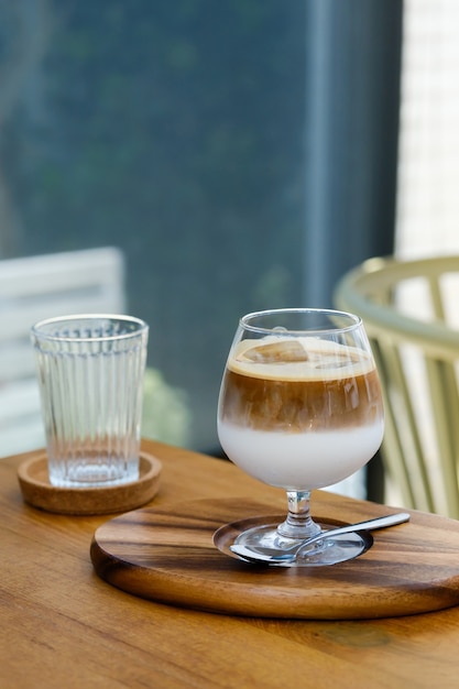 Wine glass of iced coffee two layers fresh milk and espresso short on wooden table at cafe. Refreshing summer drink concept. (close up, selective focus)