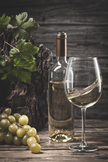 Wine glass and white wine bottle with grapes and grapevine on wooden background Vertical format