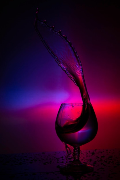 Wine glass with splashes of water on purple background