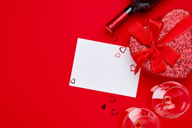 Wine, glasses and gift box in the form of heart with a red ribbon on scarlet table. Valentines day concept Top view. Top view flat lay with copy space.