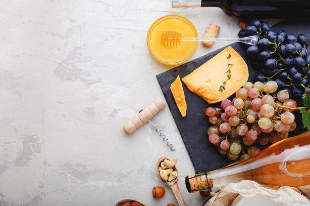 Wine snack set for food party romantic dinner. Rose champagne Red wine in bottles with variety appetizer on gray rustic concrete table. Cheese board grapes honey nuts. Flat lay with copy space.