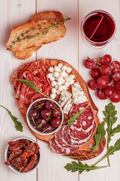 Wine snack set. Variety of cheese and meat, olives, grapes, arugula on white background