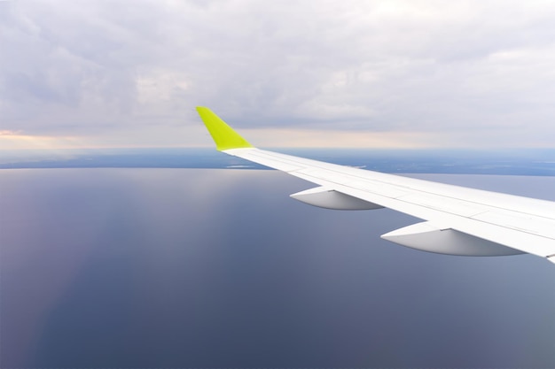 Wing of an airborne airplane ocean below the plane flies over the water clear blue sky