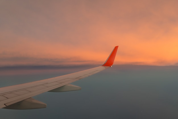 Wing airplane against the sunset sky above the cloud.