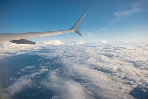 Wing of an airplane flying over white cloud in the sky during the vacation