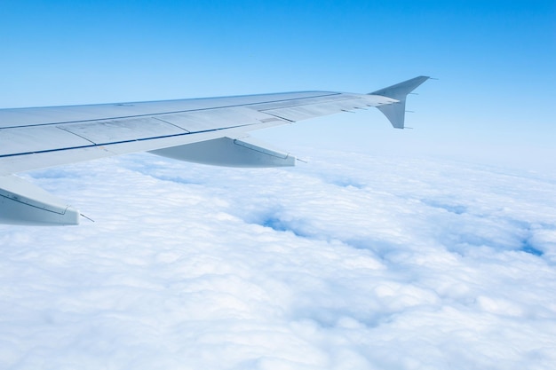 Wing of an airplane flying over white clouds and blue sky