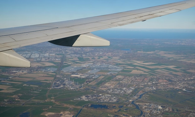 Wing of a plane as seen through an airplane window with the earth underneath