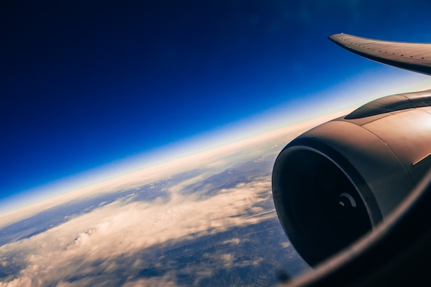 wing and turbine of the aircraft through the window against sky with clouds