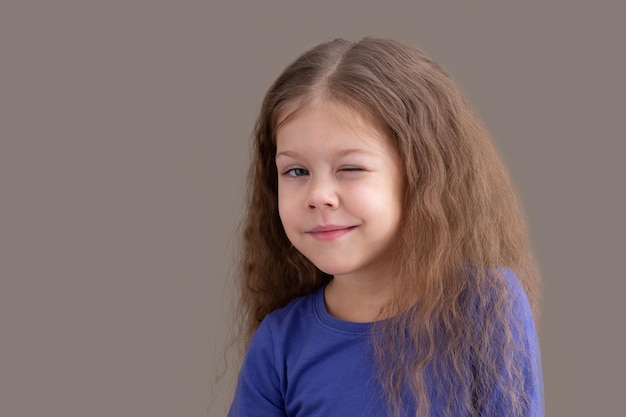 Winking child kid on brown background looking at camera portrait of caucasian little girl of 5 years in blue