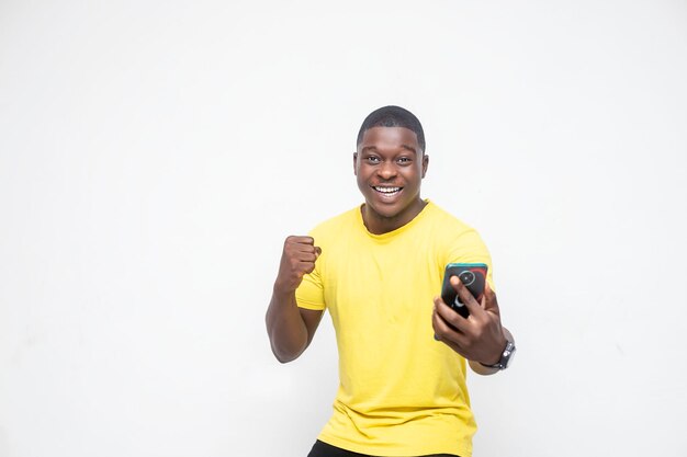 Winner mentality Portrait of attractive lucky cheerful African guy using gadget rejoicing looking at his phone isolated over white studio background