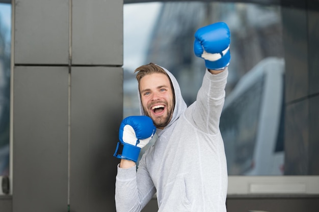 Winner takes it all. Man on smiling face posing with boxing gloves as winner, urban background. Sportsman celebrates victory. Success concept. Man motivated ambitious likes win and success.