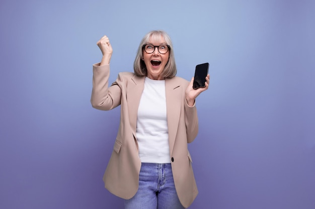 Winning mature woman in a stylish bow with a smartphone in her hands on a studio background with