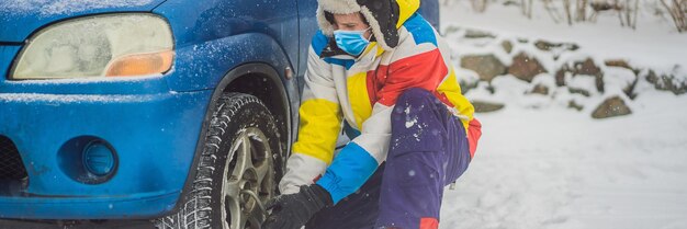 Winter accident on the road a man changes a wheel during a snowfall wear medical masks due to the