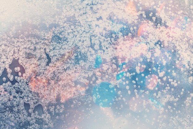 Winter background in soft pastel colors Frost and snowflakes on the window Multicolored bokeh with blur Glare through glass Background for holiday greetings with winter theme