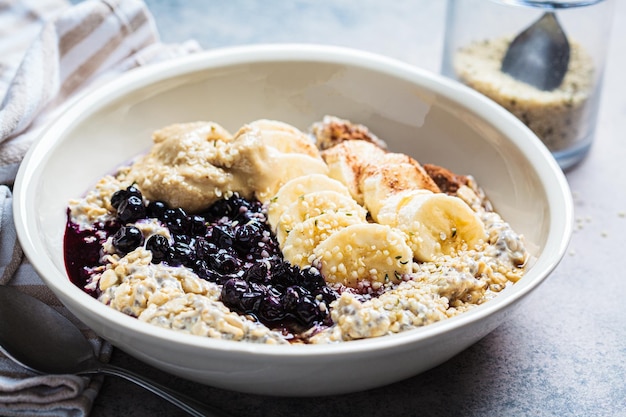 Winter breakfast concept Overnight oatmeal with banana berry chia seeds sesame tahini cinnamon and syrup in a bowl dark background