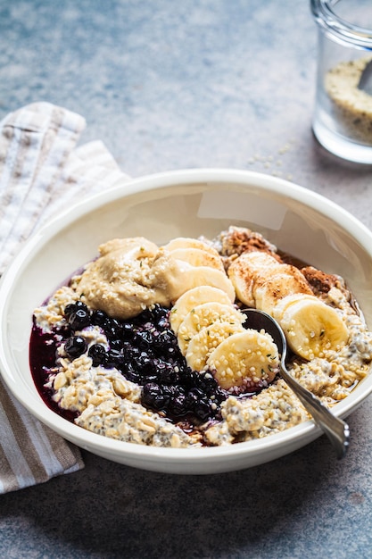 Winter breakfast concept Overnight oatmeal with banana berry chia seeds sesame tahini cinnamon and syrup in a bowl dark background