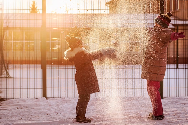 Winter Children playing with Snow in Snowy Yard. Happy Kids Have Fun Throwing Snow. Sun Light.