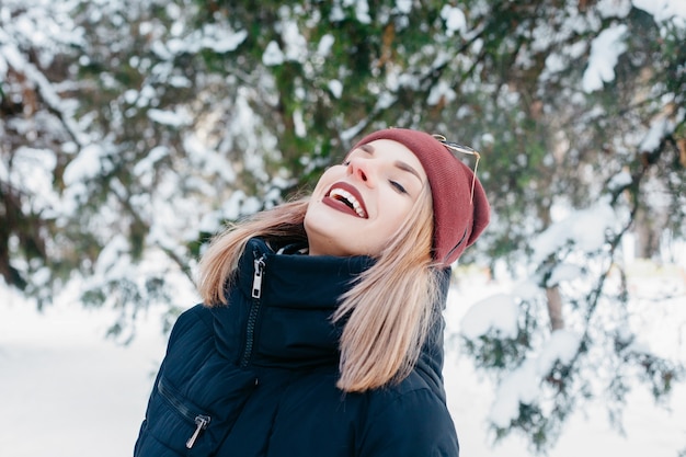 Winter, christmas, emotions, people, lifestyle and beauty concept- Christmas girl outdoor portrait. Winter woman blowing snow in a park. Flying Snowflakes. Sunny day. Backlit. Good mood