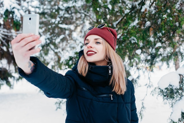 winter christmas technologies people lifestyle and beauty concept SELFI TIME Pretty brunette girl doing a selfie with her smart phoneBeautiful young woman Outdoor winter portrait