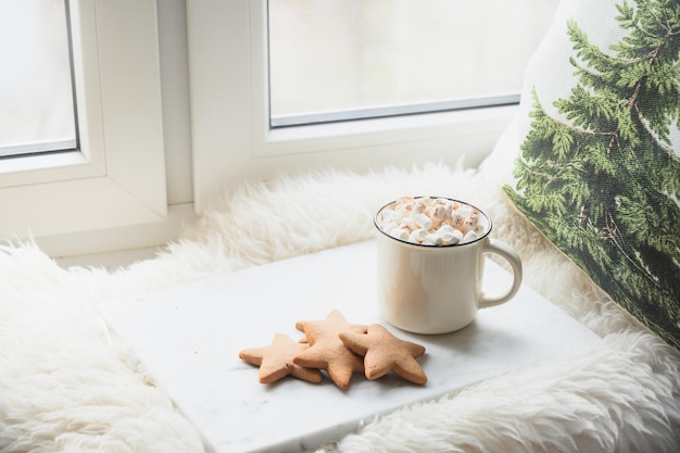 Winter coffee with marshmallow on cozy window sill with Christmas fir branches