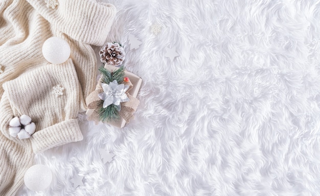 Winter cozy wall with cup of coffee, warm sweater, gift box, cotton flower and christmas ball on wool carpet wall, Top view with copy space.