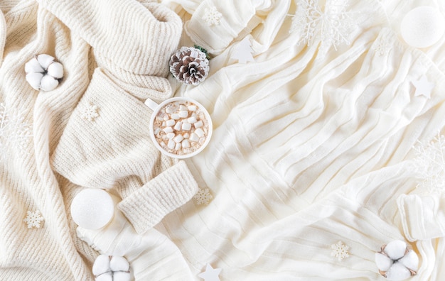 Winter cozy wall with cup of coffee, warm sweater, gift box, cotton flower and christmas ball on wool carpet wall, Top view with copy space.