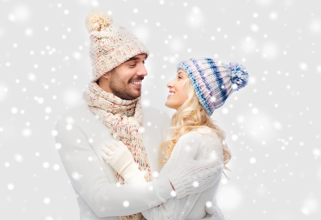 winter, fashion, couple, christmas and people concept - smiling man and woman in hats and scarf hugging