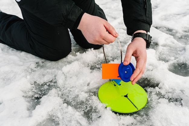 Winter fishing for pike on the imitation fish on the frozen lake Fisherman are set tackle with a flag in the ice hole on the pond Ice fisherman reeling in a fish