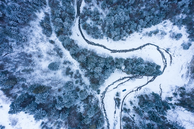 Winter forest with frosty trees and a little meandering stream, aerial view.