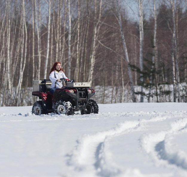 A winter forest a woman with ginger hair riding big snowmobile