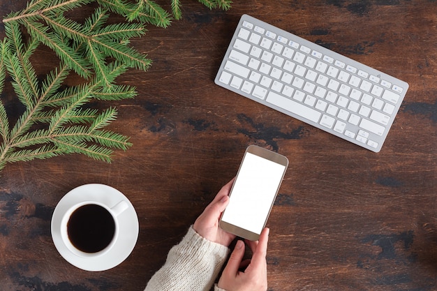 Winter green fir tree branches with cup of tea, mobile phone and white computer keyboard on wooden 