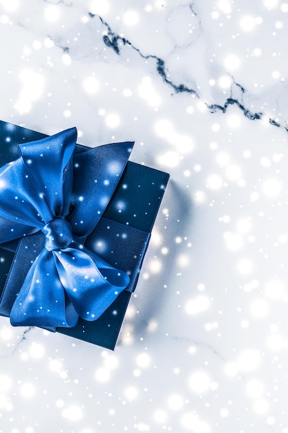 Winter holiday gift box with blue silk bow snow glitter on marble background as Christmas and New Years presents for luxury beauty brand flatlay design