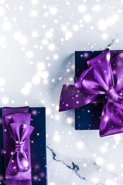 Winter holiday gift box with purple silk bow snow glitter on marble background as Christmas and New Years presents for luxury beauty brand flatlay design